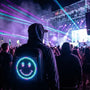 Festival goer wearing a Gelrova LED backpack with a neon pixel smiley face at a night rave, representing essential rave gear.